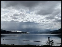 A view of the lake on a cloudy day with a rainstorm in the distance.