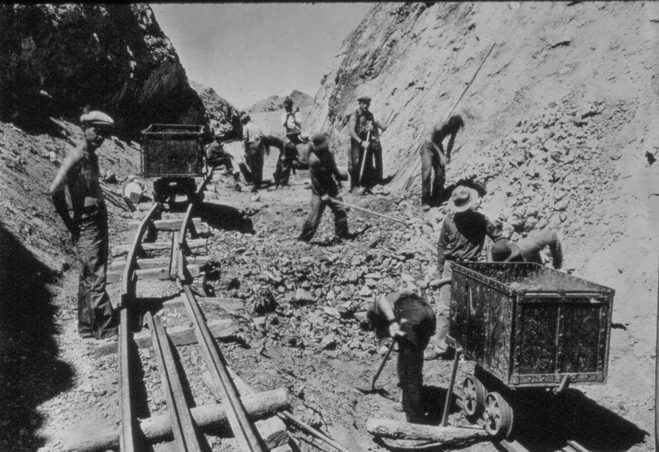 Black and white historic photo of men working along an ore cart track.