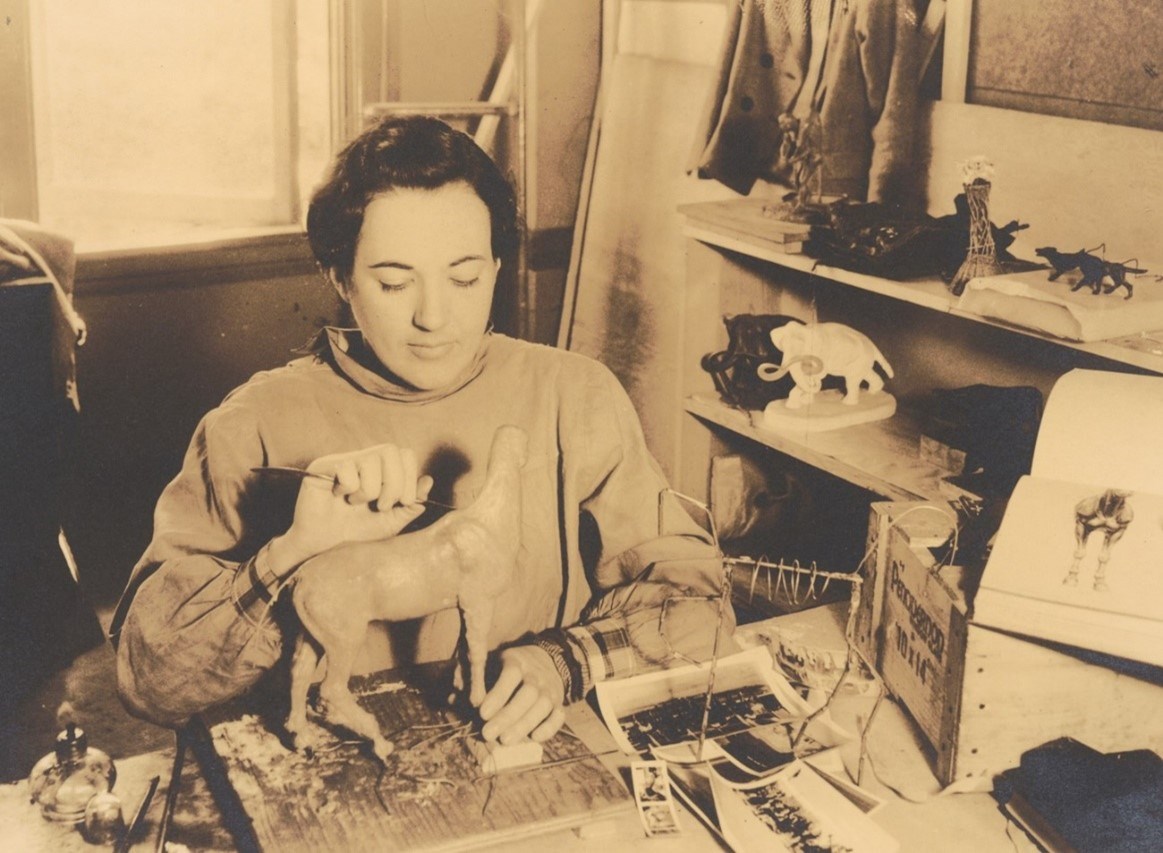 Historic photo of an artist sculpting a model of an animal.