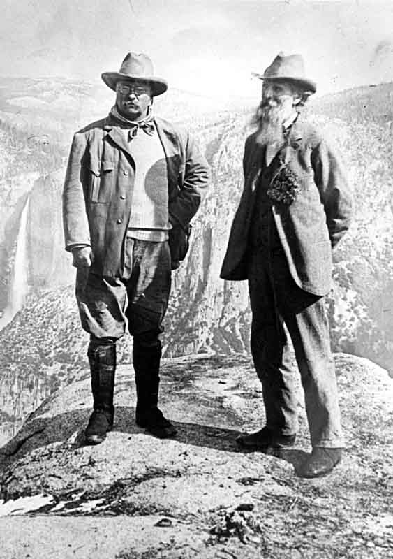 President Teddy Roosevelt and John Muir stand on a rock, with Yosemite Falls and the cliffs of Yosemite Valley in the background