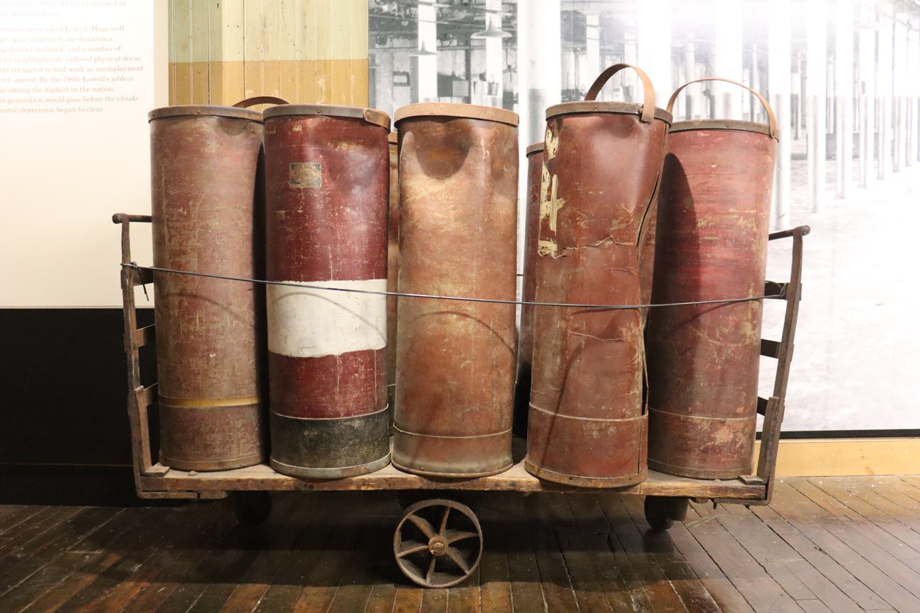 A wooden cart holding two rows of five large metal tubes. The tubes are a red brown color and some are slightly crushed