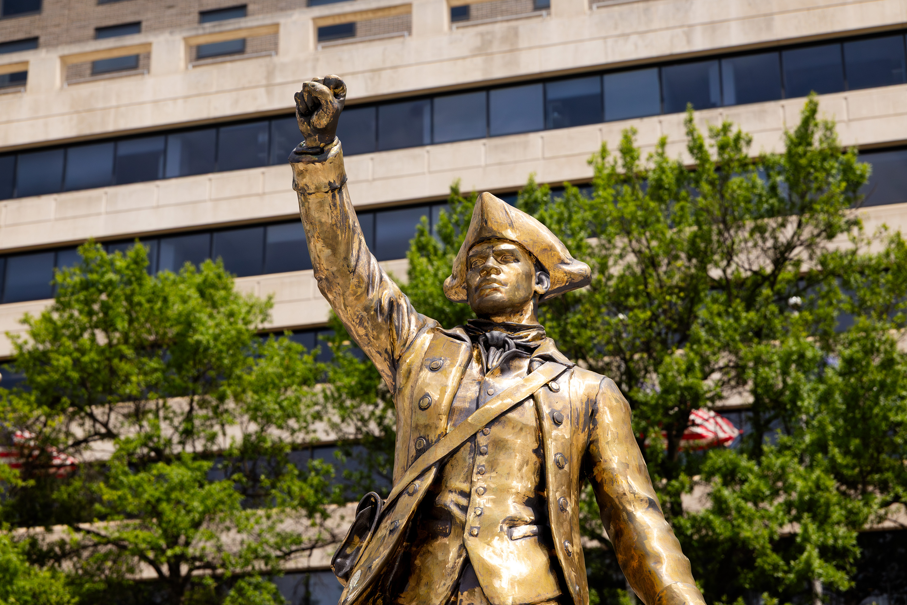 Gold toned statue of a man in a tri-corner hat raising a fist