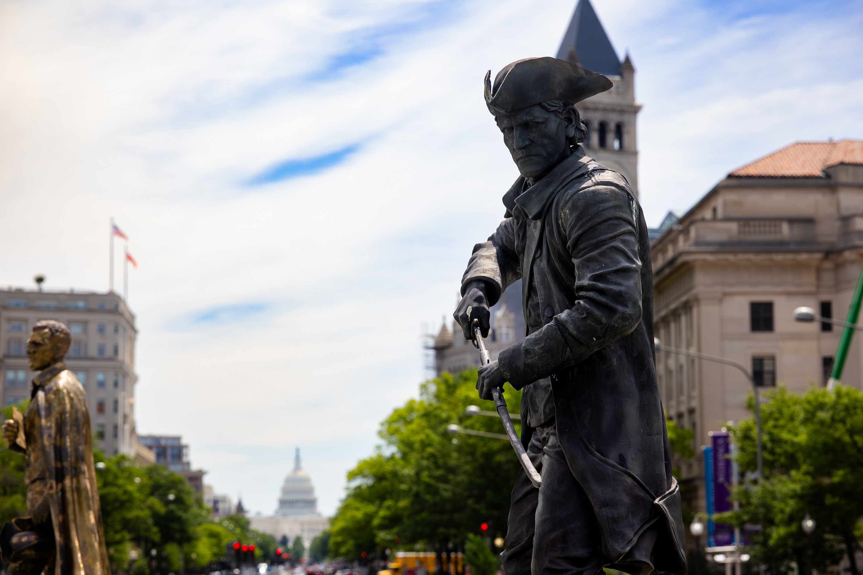 Dark bronze statue of a man in a tri-corner hat unsheathing a saber