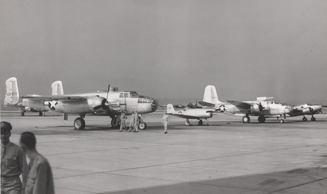 large and small planes lined up on a tarmac with a hanger in the background