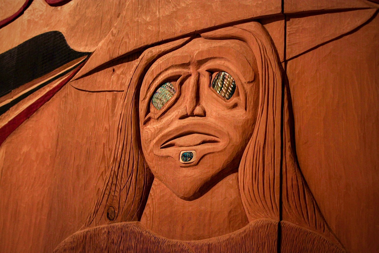 A wood carving depicting a Tlingit woman. She is carved wearing a traditional spruce root hat