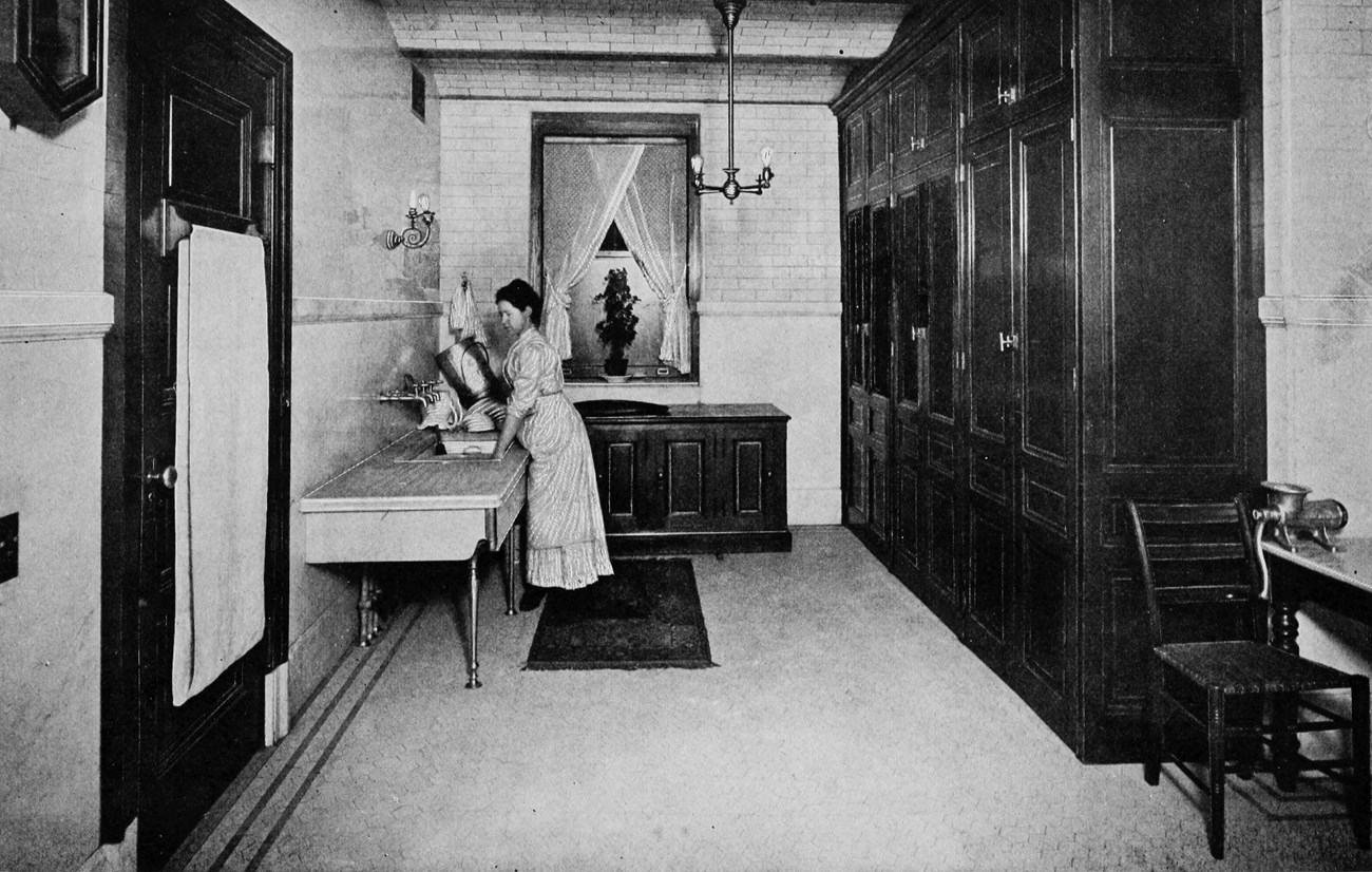 A woman washing dishes in a large scullery.