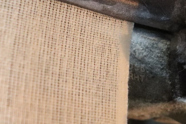close up of woven cloth. the cloth ends on the right side of the loom and the edge is a tighter material with thicker thread.