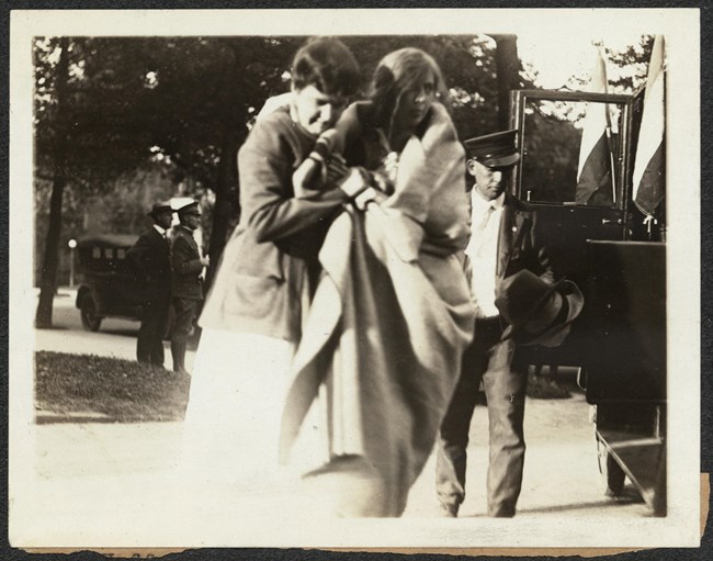 Photograph of a woman escorting Kate Heffelfinger, wrapped in blanket, outside near a car, after release from jail.