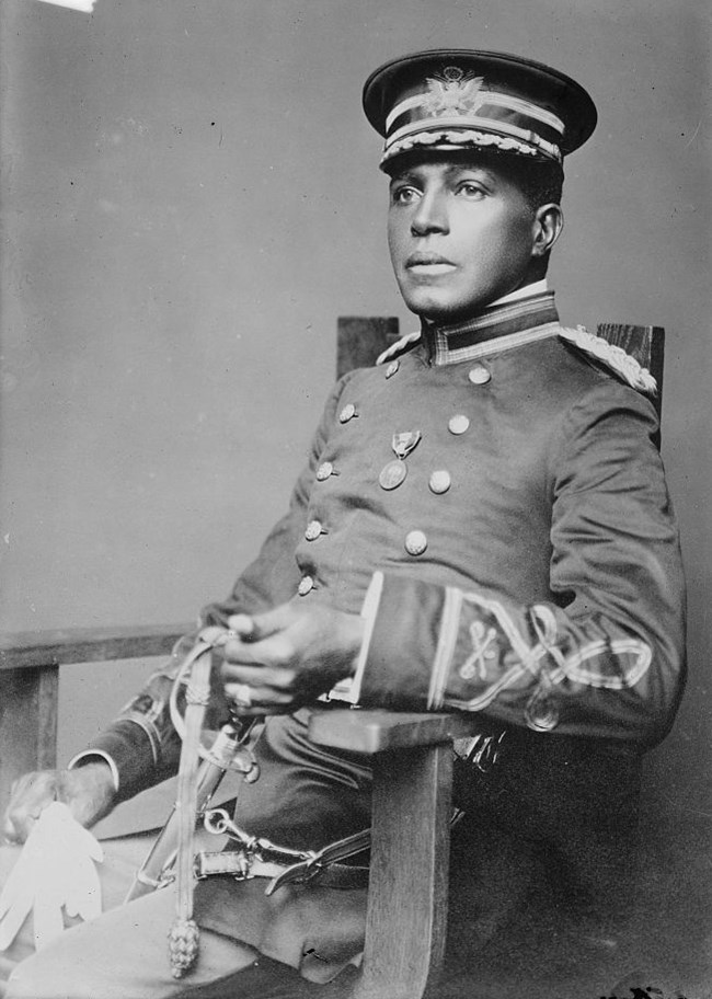 Historic black and white portrait of an African American officer sitting and holding a sword and gloves.