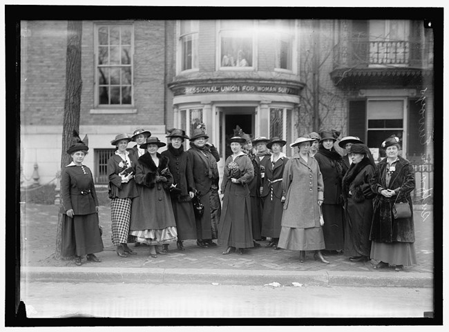 A group of women stand in front of suffragist headquarters.