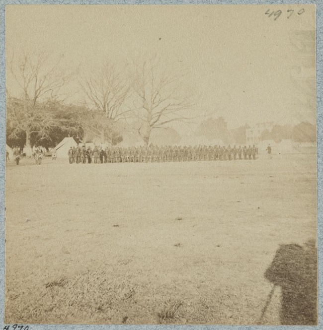faded sepia photo of men on parade ground shadow of man on horse