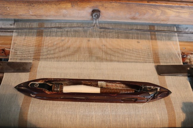 a hallow wooden vessel with pointed ends holds a bobbin full of string