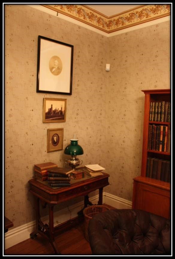 3 pictures hanging on the wall above a small table that has papers and a green lamp