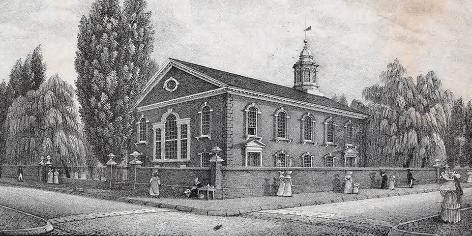 corner view of brick church with finely dressed people walking past