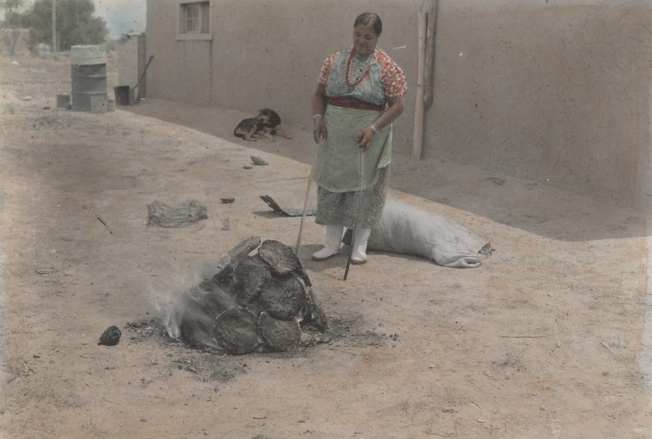 Legoria Tafoya stands outside near a fire piled high with dung.