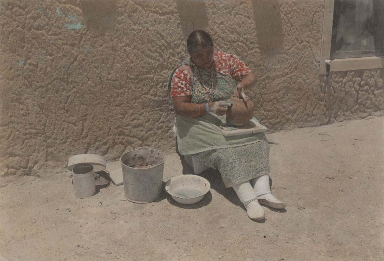 Legoria Velarde sits outside sanding the outside of an unfired clay pot