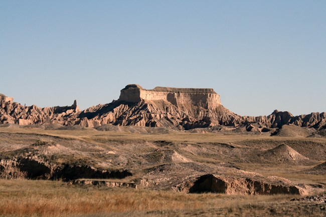 buttes stand out from a green prairie with a table-like butte in the center.