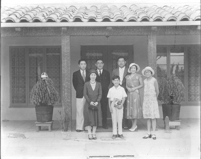 Seven people standing in front of a building. There are three men, two young women, a boy and a girl.