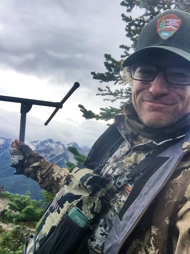 Dan holding a radio tracker high up in a snowy mountain range.