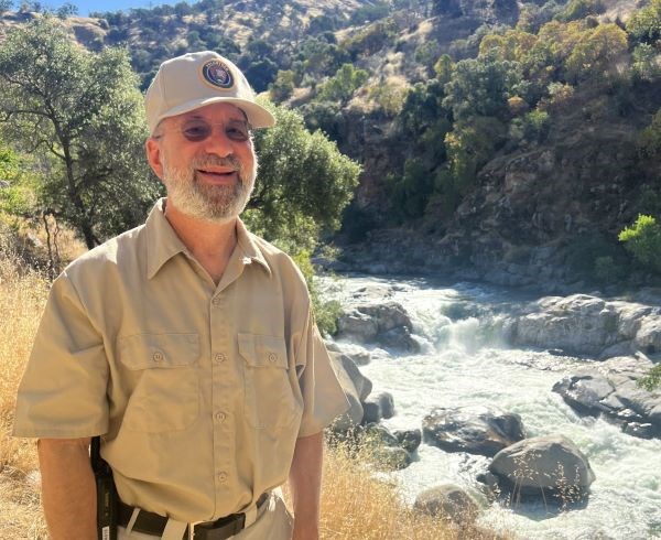 Ken Greenspan wears the Volunteer-In-Parks uniform in front of a river.