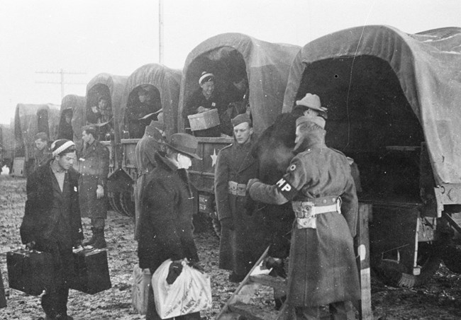 Young men are escorted by soldiers into a line of army trucks