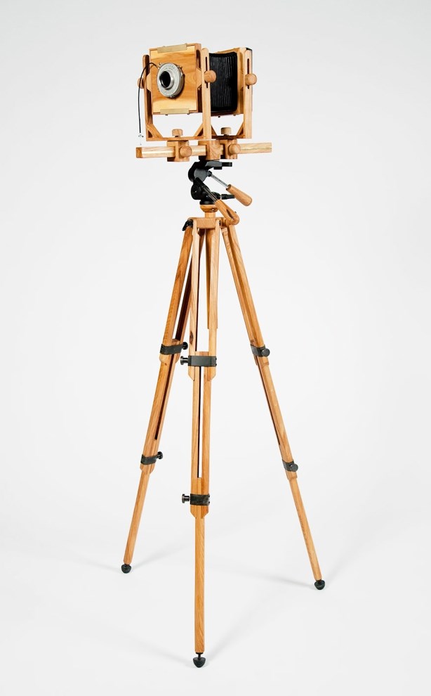 Wooden tripod with three legs, with an old school camera made of wood on top, with a wooden handle to adjust
