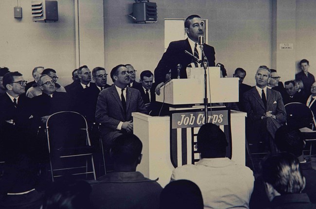 Man speaking at a podium to a room full of people