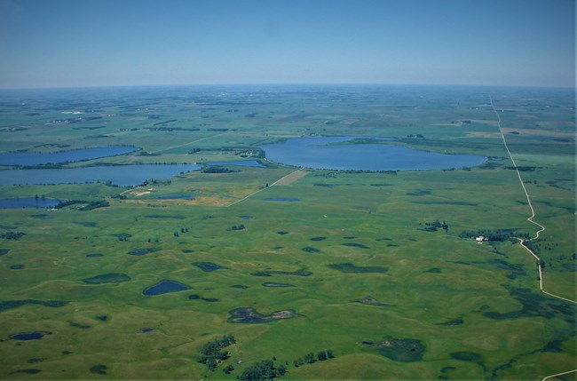 Color aerial photograph of vast green landscape pockmarked with many ponds and lakes.