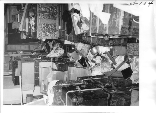Indoor stacks of luggage and boxes, some of which are broken open