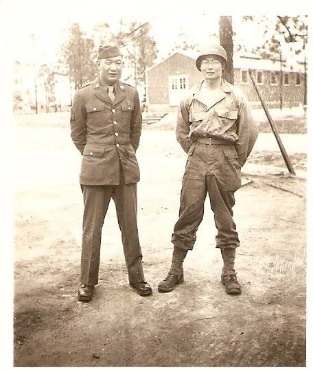 Two men in Army uniforms standing at parade rest. The man on the left is in service dress and the man on the right is in fatigues.