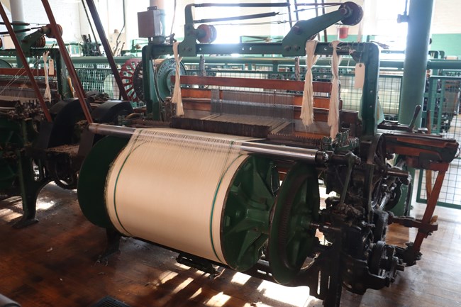 A large beam of individual threads wrapped around themselves. a row of the threads wrap over a metal bar and are fed into a machine.