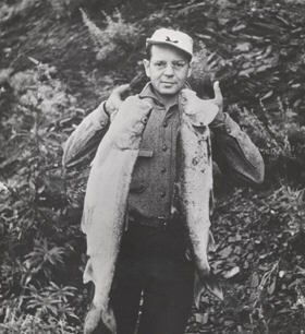 Walter Weber stands outdoors holding a large fish aloft in each hand.