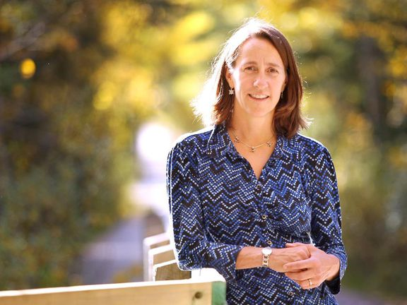 woman leans against bridge railing with a forest in the background as she looks at camera