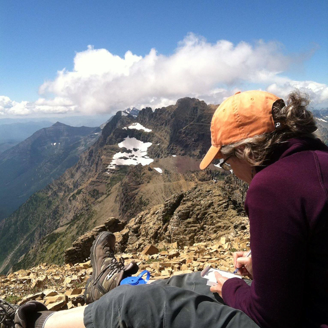 women writes in field book at the top of a mountain