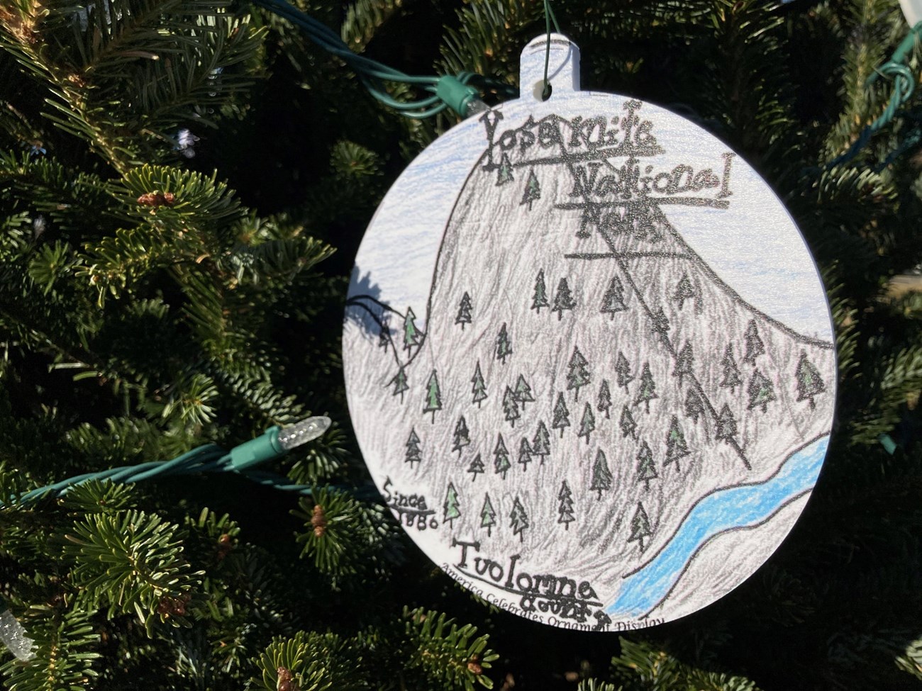 ornament with drawing of a gray tall stone, portraying yosemite. Ornament is hanging from christmas tree