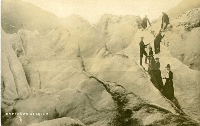 black and white photo of men and women climbing atop a glacier