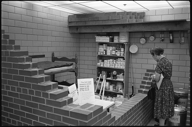 Woman views bomb shelter display which is stocked with food and other supplies