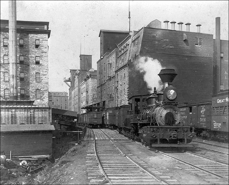 Photo of West Side Milling District, Minneapolis, ca. 1890 depicting brick buildings and steam engine on a track. (Minnesota Historical Society, photographer unknown)