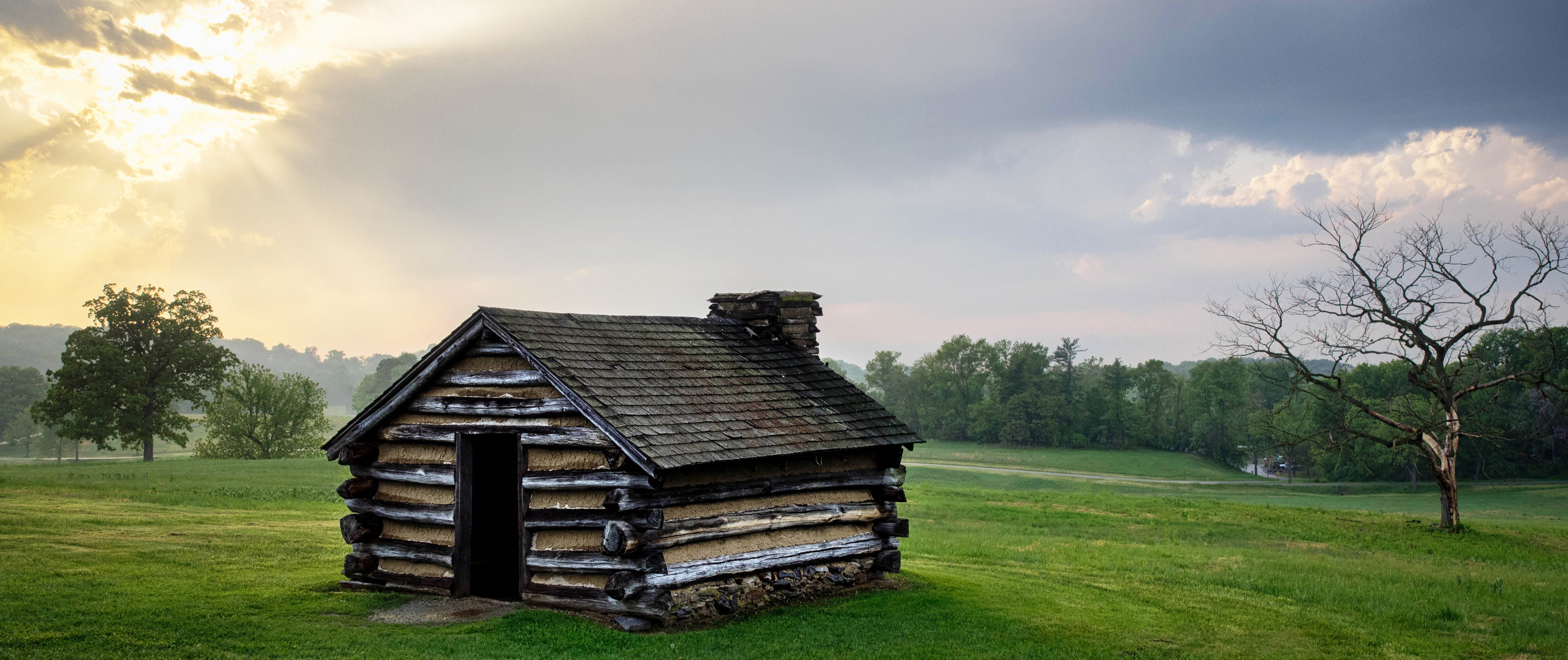 Sunrays shining down on a cabin in a green field