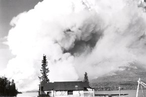 A black and white photograph of smoke from a wildfire behind a home
