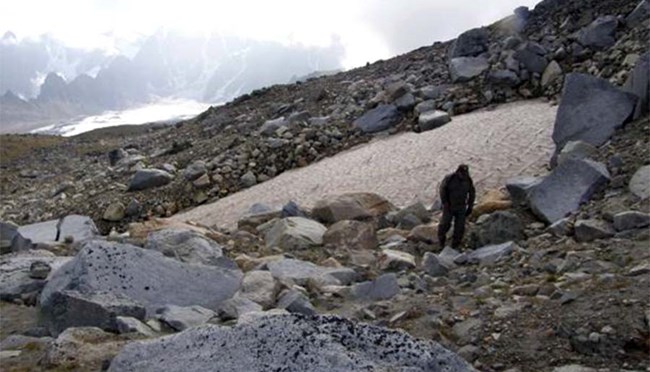 Man walking on rocky hillside by patch of snow