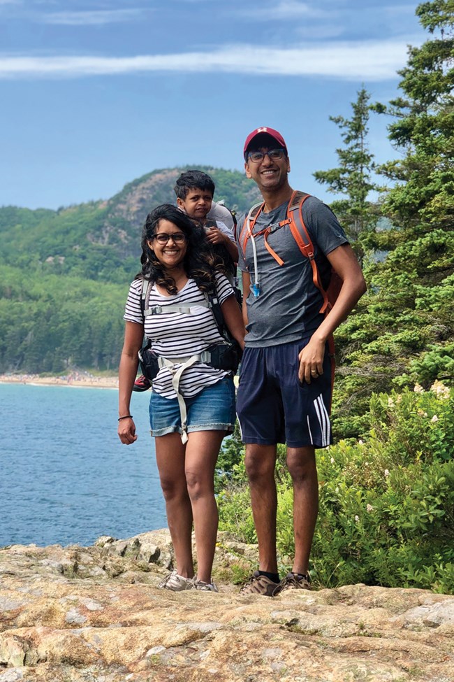 Family stands on rocky shoreline with beach and mountain in background