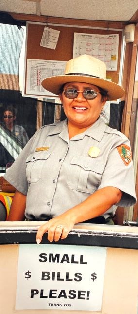 Park Ranger smiles, a sign reads small bills please.