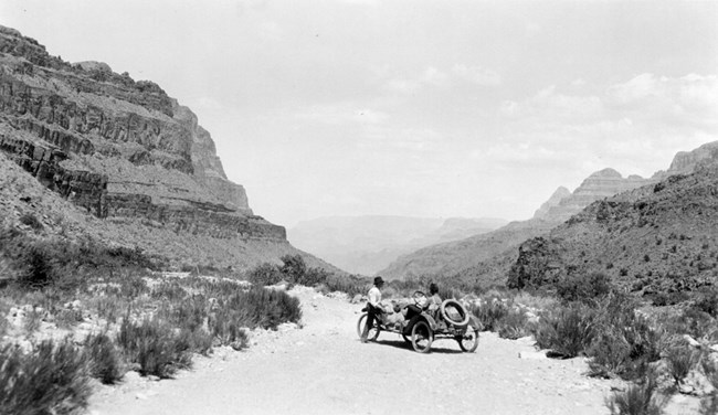 Metz car on a sandy, scrubby road between two large rocky cliffs.