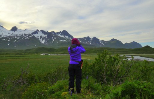 A woman looks out towards a green field and glacier