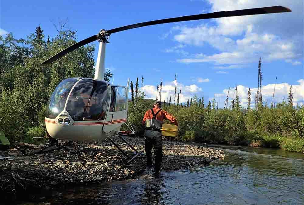 A helicopter on a river bank with scientists walking up to load it.