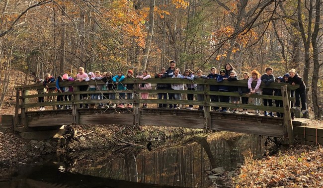 A group of students pose on a footbridge over Wolftrap Run while exploring the park's natural side during a field trip.