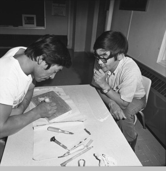 two men at a table looking at some kind of woodblock carving