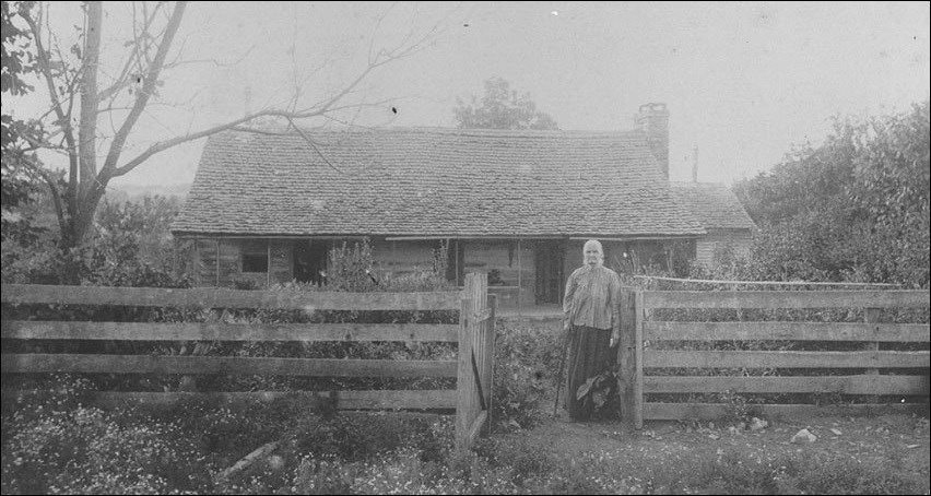 Woman in front of a log cabin.