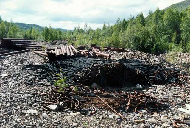large pile of metal tubes and cables or hoses on rocky ground, surrounded by forests